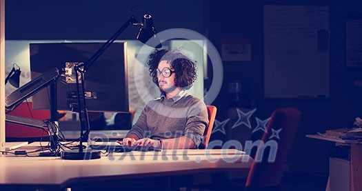 Young man working on computer at night in dark office. The designer works in the later time.