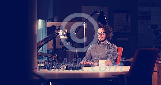 Young man working on computer at night in dark office. The designer works in the later time. Young man working on computer at night in dark office. The designer works in the later time.