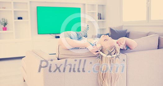 Young beautiful girl enjoying music through headphones, laying on sofa at home Young beautiful girl enjoying music through headphones, laying on sofa at home