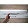 Man hand opening white drawer for cutlery, focus on steel handle of kitchen counter