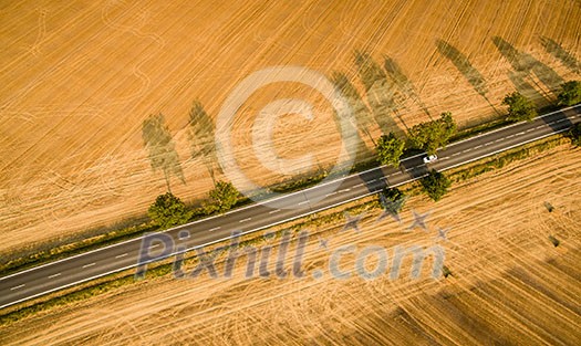 Aerial view of a country road amid fields with a car on it Aerial view of a country road amid fields with a car on it