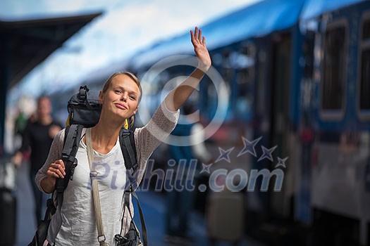 Pretty young woman boarding a train/having arrived to her destination, waiting for her friends to pick her up (color toned image)