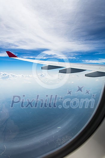 An airplane wing through airplane window with blue sky background