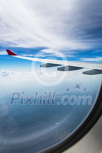 An airplane wing through airplane window with blue sky background An airplane wing through airplane window with blue sky background