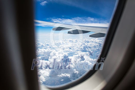 An airplane wing through airplane window with blue sky background