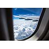 An airplane wing through airplane window with blue sky background