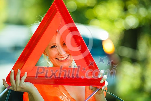Young female driver wearing a high visibility vest, calling the roadside service/assistance after her car has broken down Young female driver wearing a high visibility vest, calling the roadside service/assistance after her car has broken down