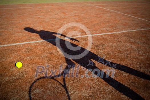 shadow of a tennis player in action on a tennis court (conceptual image with a tennis ball lying on the court and the shadow of the player positioned in a way he seems to be playing it) shadow of a tennis player in action on a tennis court (conceptual image with a tennis ball lying on the court and the shadow of the player positioned in a way he seems to be playing it)