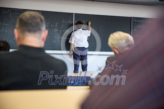 Senior male teacher teaching mathematics, writing on the blackboard