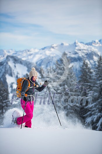 Pretty, young woman snowshoeing in high mountains, enjoying splendid winter weather with abundance of snow