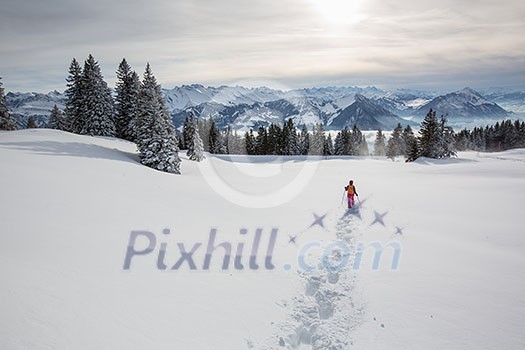 Pretty, young woman snowshoeing in high mountains, enjoying splendid winter weather with abundance of snow