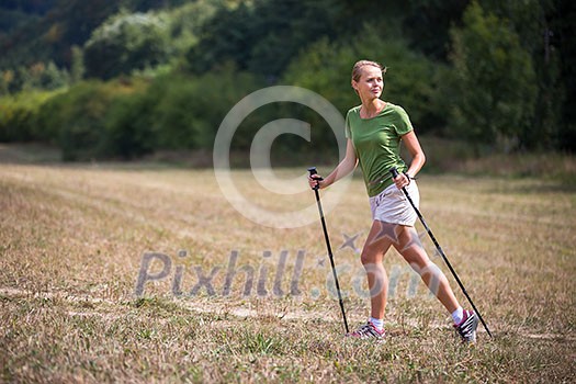 Pretty, young woman nordic walking on a forest path, taking in the fresh air, getting the daily dose of exercise