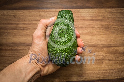 Half an avocado in a hand in front of wooden kitchen table