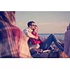 Young Couple enjoying with friends Around Campfire on The Beach At sunset drinking beer