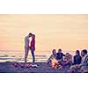 Young Couple enjoying with friends Around Campfire on The Beach At sunset drinking beer