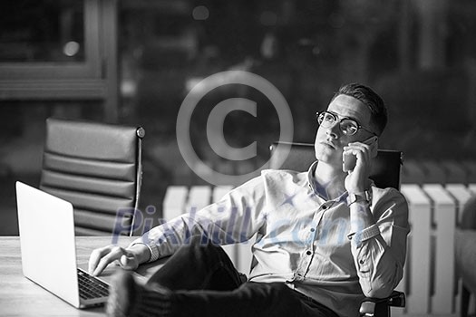 Young businessman using mobile phone while working on laptop at night in dark office. Young businessman using mobile phone while working on laptop at night in dark office.