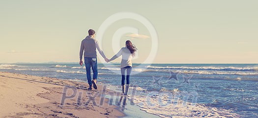 Young couple having fun walking and hugging on beach during autumn sunny day