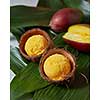 Tasty fresh yellow fruity ice cream in coconut peel with half fresh mango on green palm leaves. Summer concept