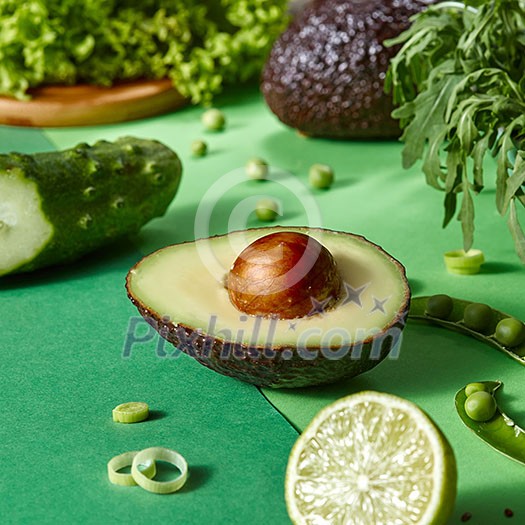 The half of avocado with bone in the focus and other green vegetables for cooking fresh natural vegetarian salad. Detox diet food. The half of avocado with bone in the focus and other green vegetables for cooking fresh natural vegetarian salad. Detox diet food.