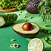 The half of avocado with bone in the focus and other green vegetables for cooking fresh natural vegetarian salad. Detox diet food.