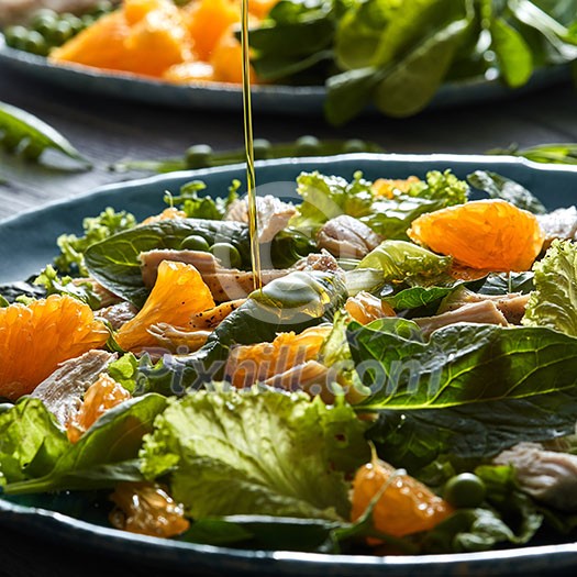 Delicious natural salad with fresly picked green vegetables, spinach, green peas, lettuce, orange fruit, chicken meat in a blue plate with olive oil pours into plate.