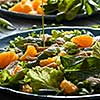 Delicious natural salad with fresly picked green vegetables, spinach, green peas, lettuce, orange fruit, chicken meat in a blue plate with olive oil pours into plate.