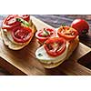 Caprese bruschetta toasts with mozzarella, cherry tomatoes and fresh garden basil on a woden background. Italian traditional healthy eating. Healthy organic snack
