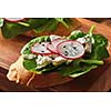 Ciabatta toasts with soft cottage cheese, slices of radish, fresh spinach, flax seeds on wooden background. Healthy vegetarian snack.