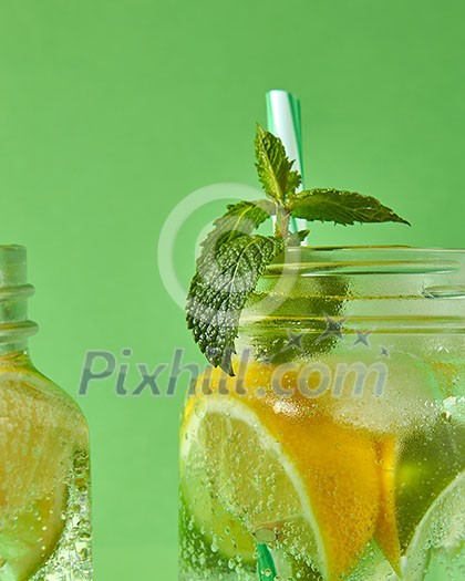 A close-up of a sprig of green mint in focus in a glass jar with cold natural handmade lemonade on green background. Concept of cold alcoholic or non-alcoholic summer drinks. A close-up of a sprig of green mint in focus in a glass jar with cold natural handmade lemonade on green background. Concept of cold alcoholic or non-alcoholic summer drinks.