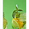 A close-up of a sprig of green mint in focus in a glass jar with cold natural handmade lemonade on green background. Concept of cold alcoholic or non-alcoholic summer drinks.