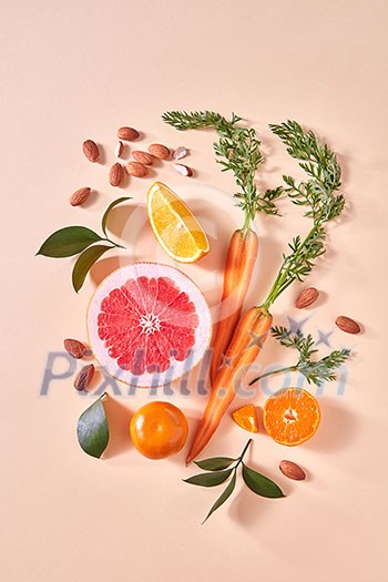 Carrot, slices of orange and grapefruit, almond, mandarins, green leaf - on a paper background. Concept of colorful organic food. Flat lay