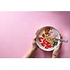 Healthy smoothie in white bowl with natural fruits, oat flakes and biscuits with woman's hands holding a bowl on pink background. Superfoods, natural detox, diet and healthy food. Flat lay