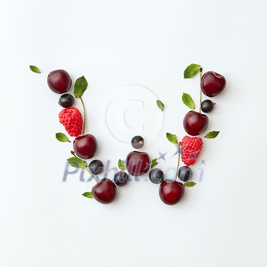 Letter W english alphabet in the form of a pattern of natural organic berries - ripe fresh raspberry, black currant, cherry, green mint leaf isolated on a white background. Top view.