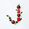 Letter J english alphabet in the form of a pattern of natural organic berries - ripe fresh raspberry, black currant, cherry, green mint leaf isolated on a white background. Top view.