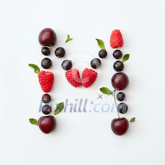 Letter M english alphabet in the form of a pattern of natural organic berries - ripe fresh raspberry, black currant, cherry, green mint leaf isolated on a white background. Top view.
