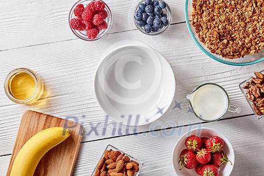 Empty plate, organic granola, banana, honey, milk, berries and almonds on a white wooden table with copy space. Ingredients for a healthy breakfast, step by step recipe. Top view