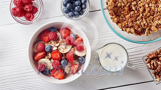 White ceramic bowl with natural organic berries, fruits, nuts, milk, muesli on wthite wooden background. Concept of natural healthy organic food. Top view.