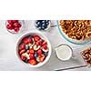 White ceramic bowl with natural organic berries, fruits, nuts, milk, muesli on wthite wooden background. Concept of natural healthy organic food. Top view.