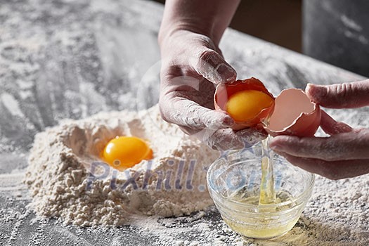 A women's hands baker shares an egg on the background of a kitchen table with flour. The concept of a step-by-step preparation of a dough for baking A women's hands baker shares an egg on the background of a kitchen table with flour. The concept of a step-by-step preparation of a dough for baking