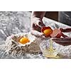 A women's hands baker shares an egg on the background of a kitchen table with flour. The concept of a step-by-step preparation of a dough for baking