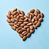 Dried almonds in the shape of heart on a blue paper background flat lay. Organic food