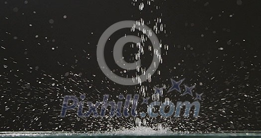 Running water falls from above on a flat surface with splashes and droplets of water, scattering in different directions against a black background. Slow motion. Full HD video, 240fps, 1080p