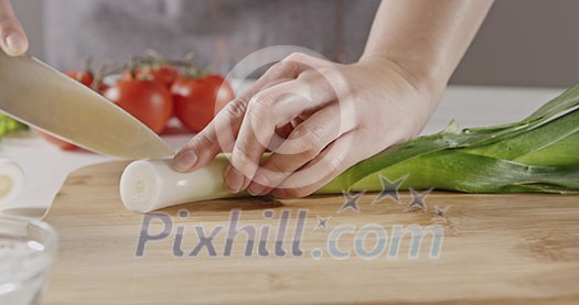 Close-up background with red ripe tomatoes, organic greens on white table. Chef in an apron slices green leek on a wooden cutting board for cooking a salad. Slow motion video in 4K