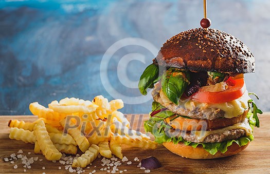 Large juicy burger with two cutlets and french fries on a wooden table