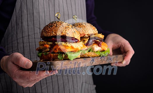 Chicken burger with pineapple. Men's hands hold a tray with a cheeseburger. Chicken burger with pineapple. Men's hands hold a tray with a cheeseburger.