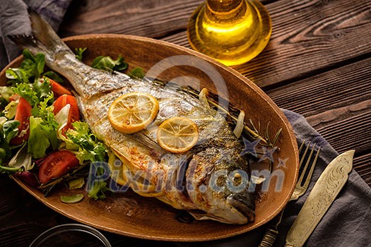 Grilled Dorado with lemon, thyme, rosemary and fresh salad on the wooden table