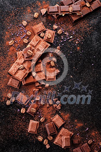 Broken chocolate pieces and cocoa powder on marble. The chunks of chocolate over dark background