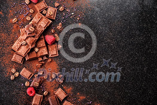 Broken chocolate pieces and cocoa powder on marble. The chunks of chocolate over dark background Broken chocolate pieces and cocoa powder on marble. The chunks of chocolate over dark background