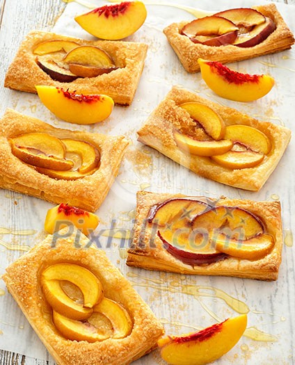 Tasty fresh homemade puff pastry with peach and honey on the white wooden table.
