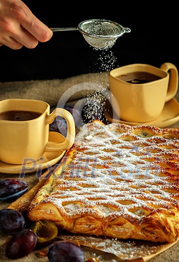 The girl sprinkles with sugar powder an apple strudel made of puff pastry.